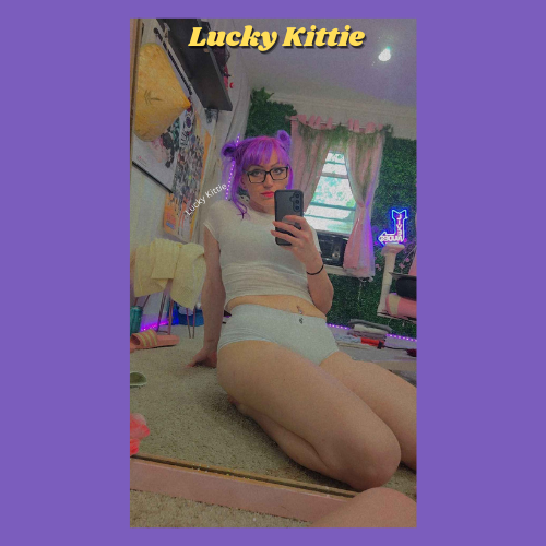 Indiecammodels FemDom cam model Lucky Kittie sitting on the floor in panties and a tee shirt with her purple hair tied back and sexy glasses on.