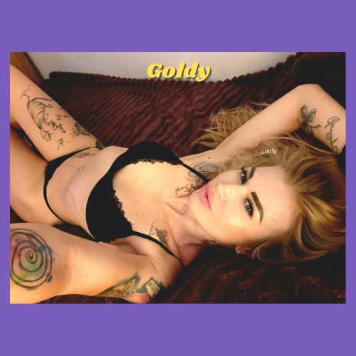 IndieCamModels Girl Next Door Cam Model Goldy IndieCamFans lounging in a black bra and panty set with her long hair splayed out on the pillow.